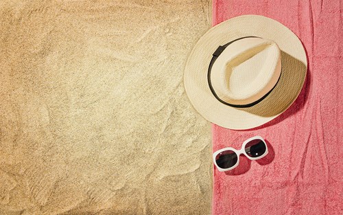 Hat and sunglasses on light red beach towel